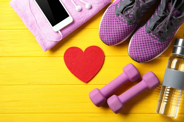 Cosas del gimnasio, teléfono y corazón rojo sobre fondo de madera de color. Concepto de entrenamiento cardiovascular — Foto de Stock