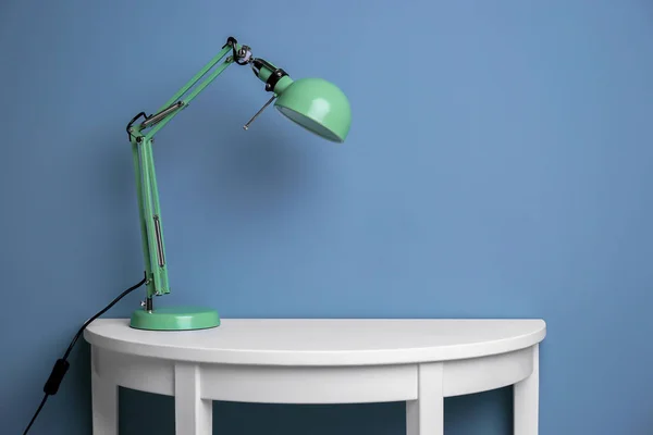 Элегантная лампа на столе рядом с цветной стеной — стоковое фото