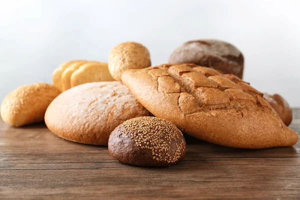 Variety of fresh tasty bread on wooden table against light background — Stock Photo, Image