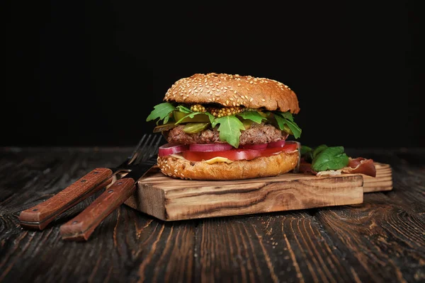 Hamburger savoureux sur planche en bois sur fond sombre — Photo
