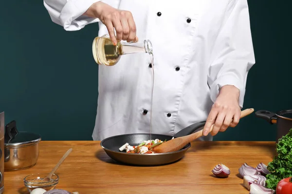 Шеф-повар в униформе добавляет масло к вкусному блюду на столе, крупным планом — стоковое фото
