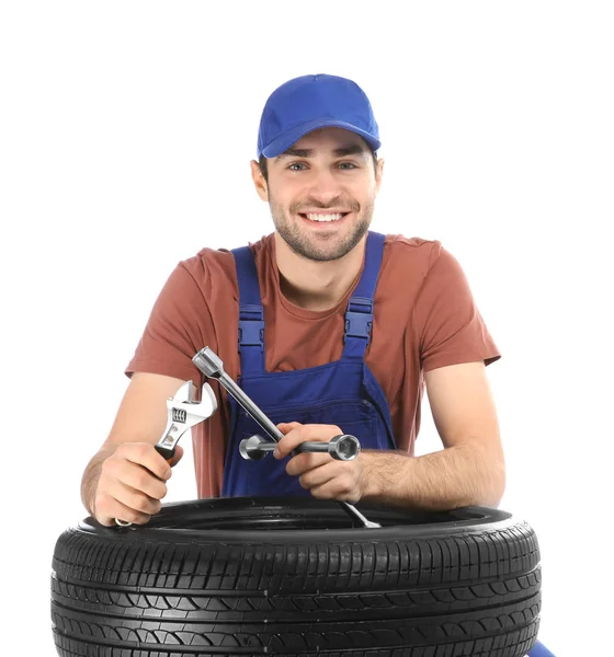 Jovem mecânico em uniforme com pneu de carro no fundo branco — Fotografia de Stock