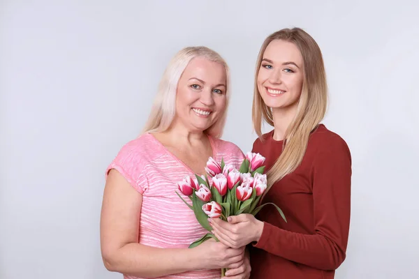 Jonge dochter en moeder met boeket bloemen op lichte achtergrond — Stockfoto