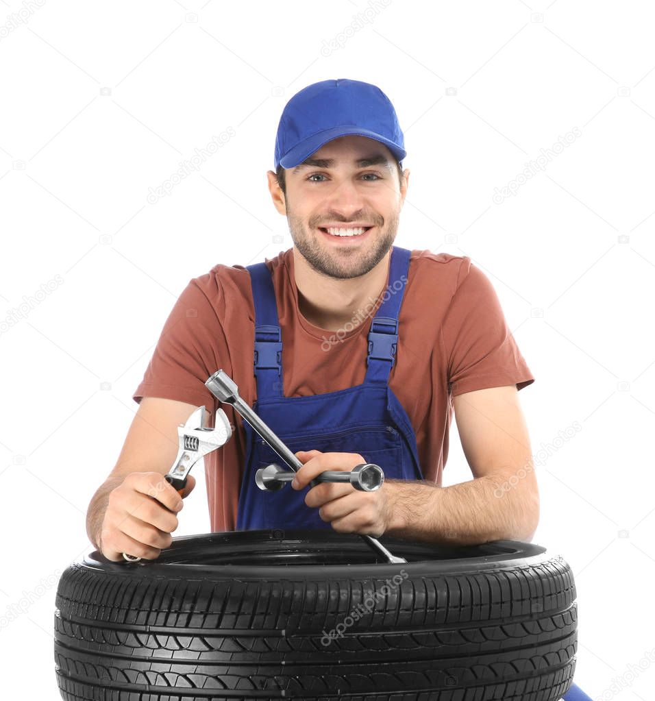Young mechanic in uniform with car tire on white background
