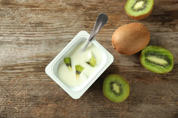 Plastic beker met lekker kiwi yoghurt op houten tafel — Stockfoto