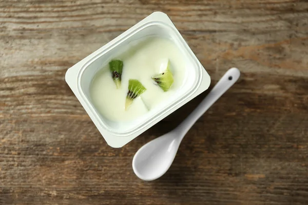 Tazza di plastica con delizioso yogurt kiwi sul tavolo di legno — Foto Stock