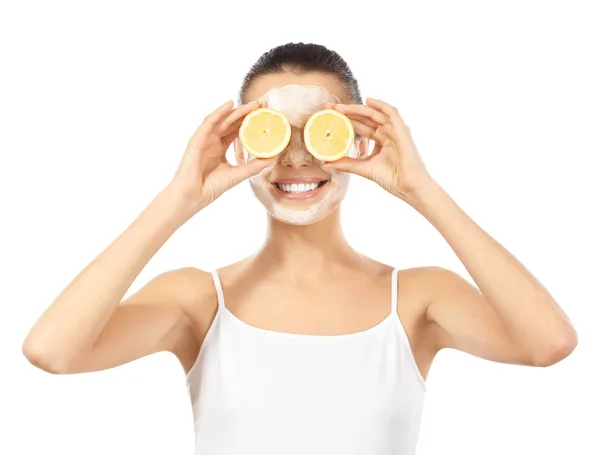 Wanita muda cantik dengan masker wajah dan irisan lemon matang di latar belakang putih — Stok Foto