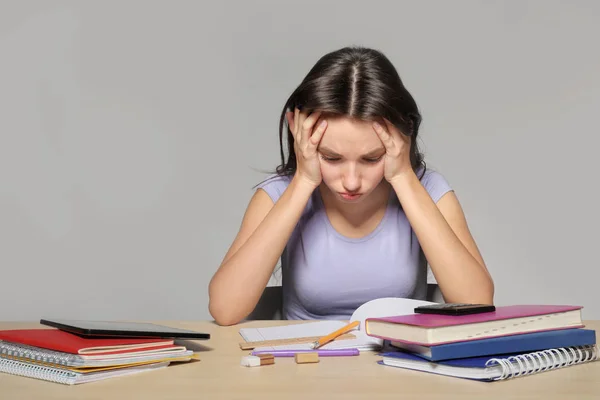 Tired teenager girl doing homework against grey background — Stock Photo, Image