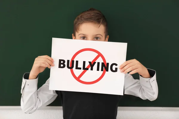 Niño pequeño sosteniendo cartel con la palabra cruzada "Bullying" en el aula —  Fotos de Stock