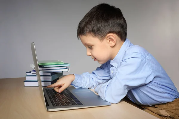 Söt liten pojke med laptop medan du gör läxor mot grå bakgrund — Stockfoto