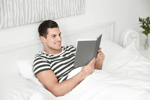 Młody przystojny mężczyzna czytania książki w łóżku w domu — Zdjęcie stockowe