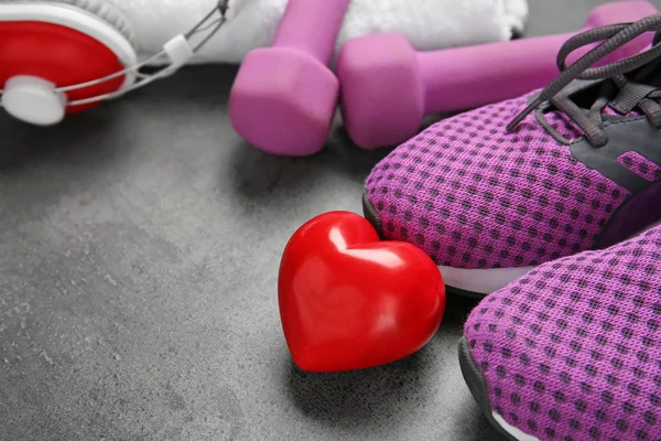 Turnsachen und rotes Herz auf grauem Hintergrund. Cardio-Trainingskonzept — Stockfoto