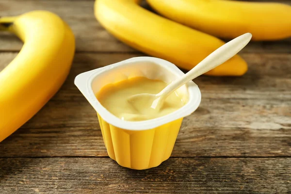 Plastikbecher mit leckerem Bananenjoghurt auf Holztisch — Stockfoto