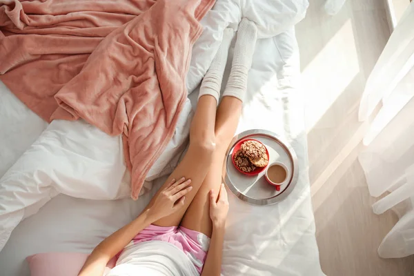 Νεαρή γυναίκα και δίσκος με νόστιμο πρωινό στο κρεβάτι στο σπίτι — Φωτογραφία Αρχείου