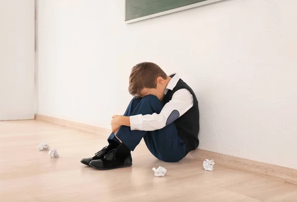 Zdenerwowany mały chłopiec siedzi na podłodze w pomieszczeniu. Zastraszanie w szkole — Zdjęcie stockowe
