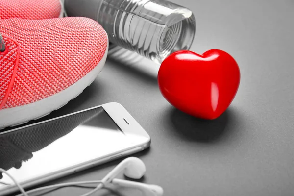 Cosas del gimnasio, teléfono y corazón rojo sobre fondo gris. Concepto de entrenamiento cardiovascular — Foto de Stock