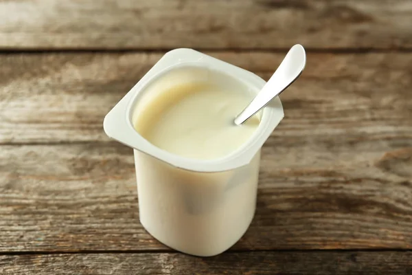 Plastic cup with yummy vanilla yogurt on wooden table — Stock Photo, Image