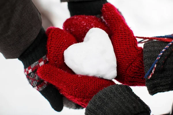 Young loving couple holding heart made of snow, closeup