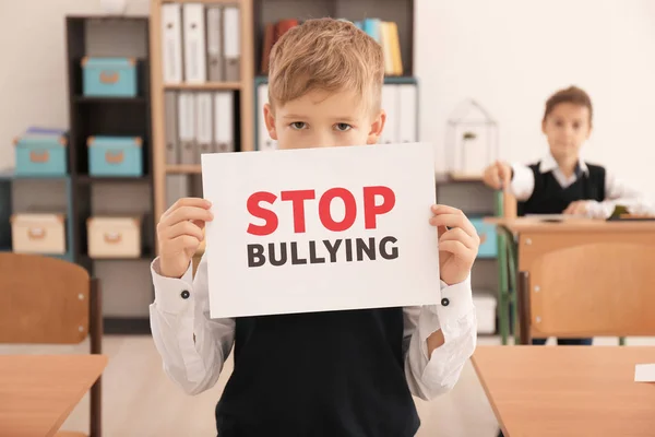 Niño pequeño sosteniendo el cartel con las palabras "Stop bullying" en el aula — Foto de Stock