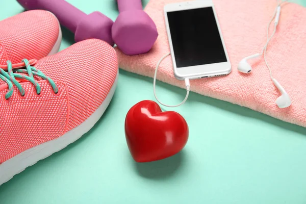 Cosas del gimnasio, teléfono y corazón rojo sobre fondo de color. Concepto de entrenamiento cardiovascular — Foto de Stock
