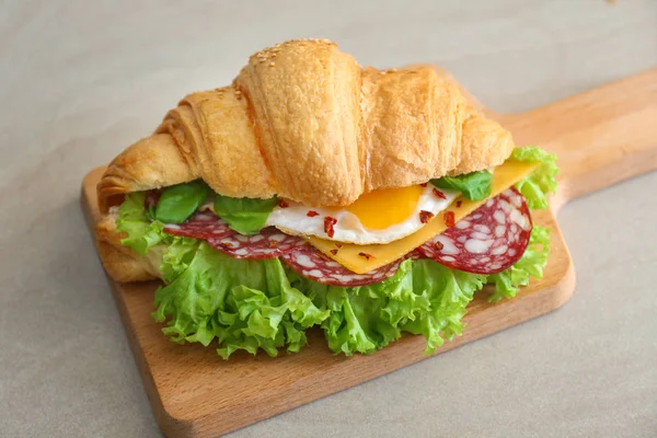 Wooden board with tasty croissant sandwich on table — Stock Photo, Image