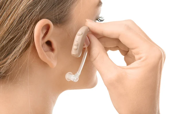 Молодая женщина кладет слуховой аппарат в ухо на белом фоне — стоковое фото