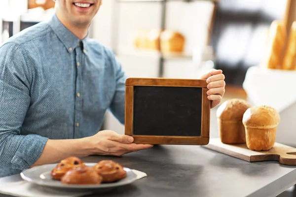 Hombre sosteniendo mini pizarra en la panadería. Dueño de pequeña empresa — Foto de Stock