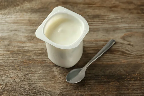 Copo de plástico com iogurte de baunilha gostoso na mesa de madeira — Fotografia de Stock