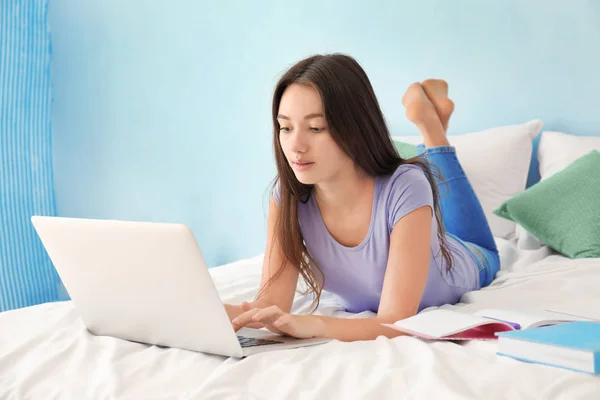 Cute teenager girl using laptop while doing homework in bedroom — Stock Photo, Image