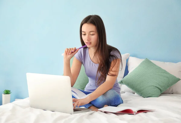 Cute teenager girl using laptop while doing homework in bedroom — Stock Photo, Image