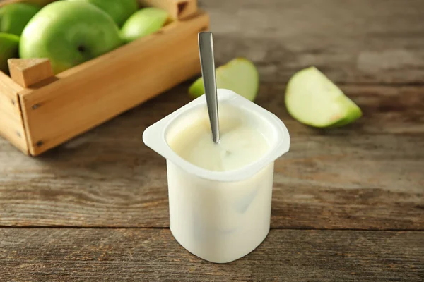 Пластиковая чашка с вкусным яблочным йогуртом на деревянном столе — стоковое фото