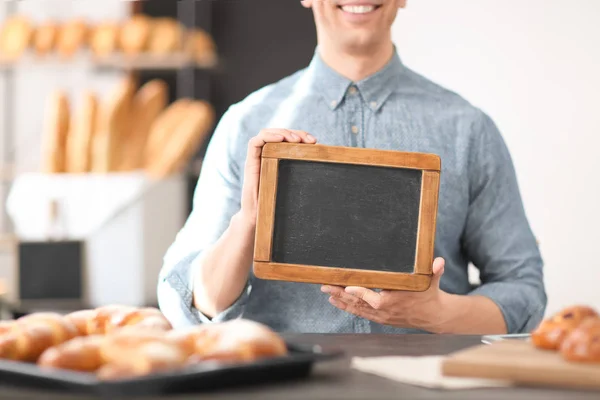 Hombre sosteniendo mini pizarra en la panadería. Dueño de pequeña empresa — Foto de Stock