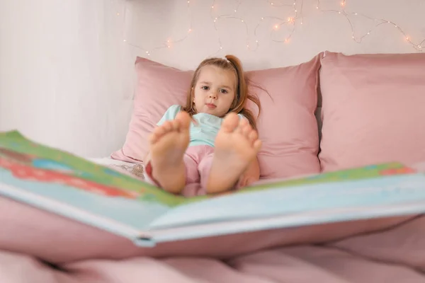 Söt liten flicka med boken vilar på sängen hemma — Stockfoto