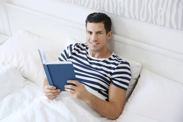 Giovane bell'uomo che legge libro a letto a casa — Foto Stock