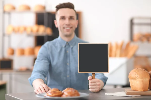 Portrait of young man with mini chalkboard in bakery. Small business owner — Stock Photo, Image