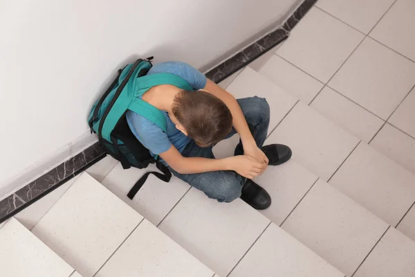 Sad little boy with backpack sitting on stairs. Bullying in school — Stock Photo, Image