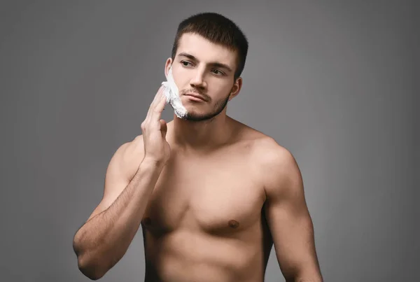 Hombre joven aplicando espuma de afeitar — Foto de Stock