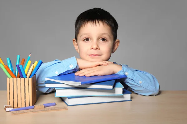 Cute little boy with lot of homework to do against grey background — Stock Photo, Image