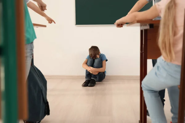 Menino intimidado sentado no chão em sala de aula — Fotografia de Stock
