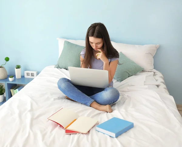 Милая девочка-подросток с ноутбука во время выполнения домашней работы в спальне — стоковое фото