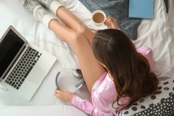 Giovane donna con tazza di caffè e laptop sul letto a casa — Foto Stock