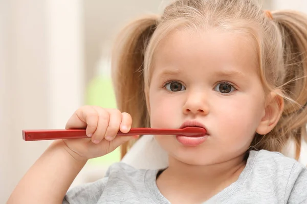 Маленька дівчинка чистить зуби на розмитому фоні — стокове фото