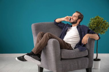 Yakışıklı adam evde rahat koltukta otururken cep telefonu üzerinde konuşurken
