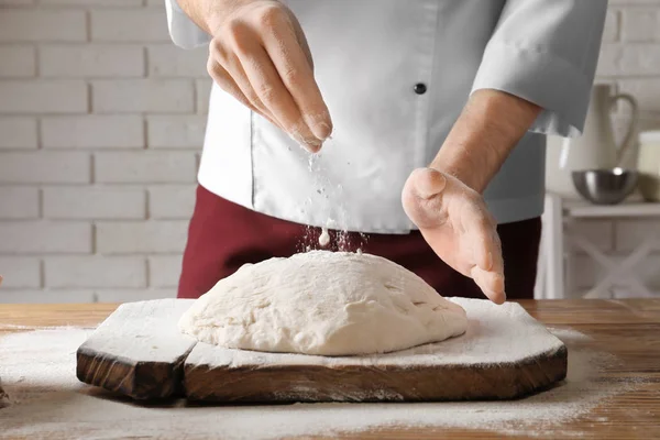 Man sprinkling dough with flour on table