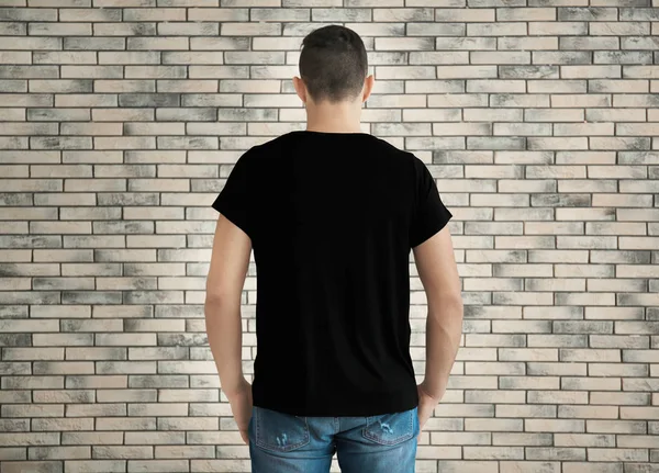 年轻男子穿着时髦的 T恤衫 在砖墙背景 设计样机 — 图库照片