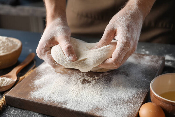 Man kneading dough on wooden board sprinkled with flour