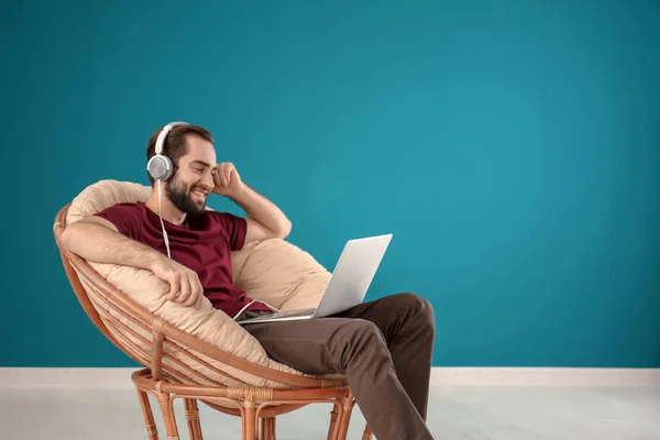 Przystojny Mężczyzna Laptopa Słuchanie Muzyki Siedząc Wygodnym Fotelu Kolorów Muru — Zdjęcie stockowe