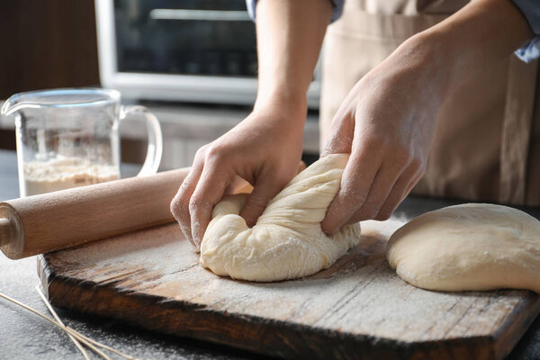 Woman kneading dough on wooden board sprinkled with flour