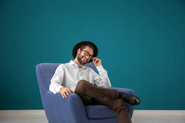 Bonito Homem Sentado Poltrona Confortável Contra Parede Cor — Fotografia de Stock