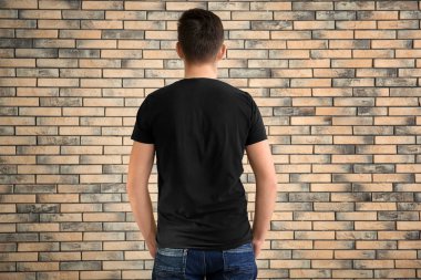 Tuğla duvar arka plan üzerinde şık tişört genç adam. Mockup tasarım için